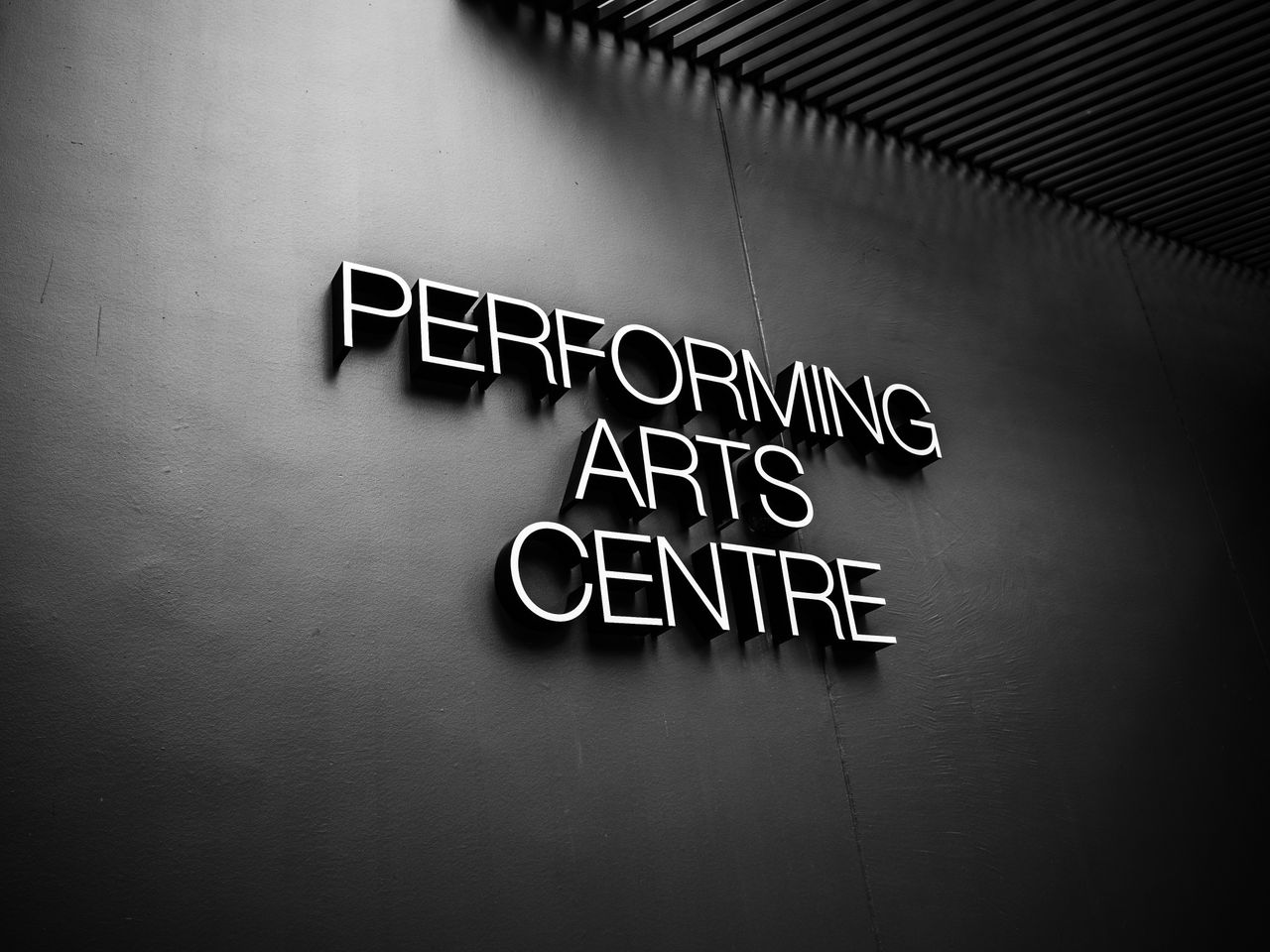 Monochrome image of a performing arts centre sign on a dark wall.